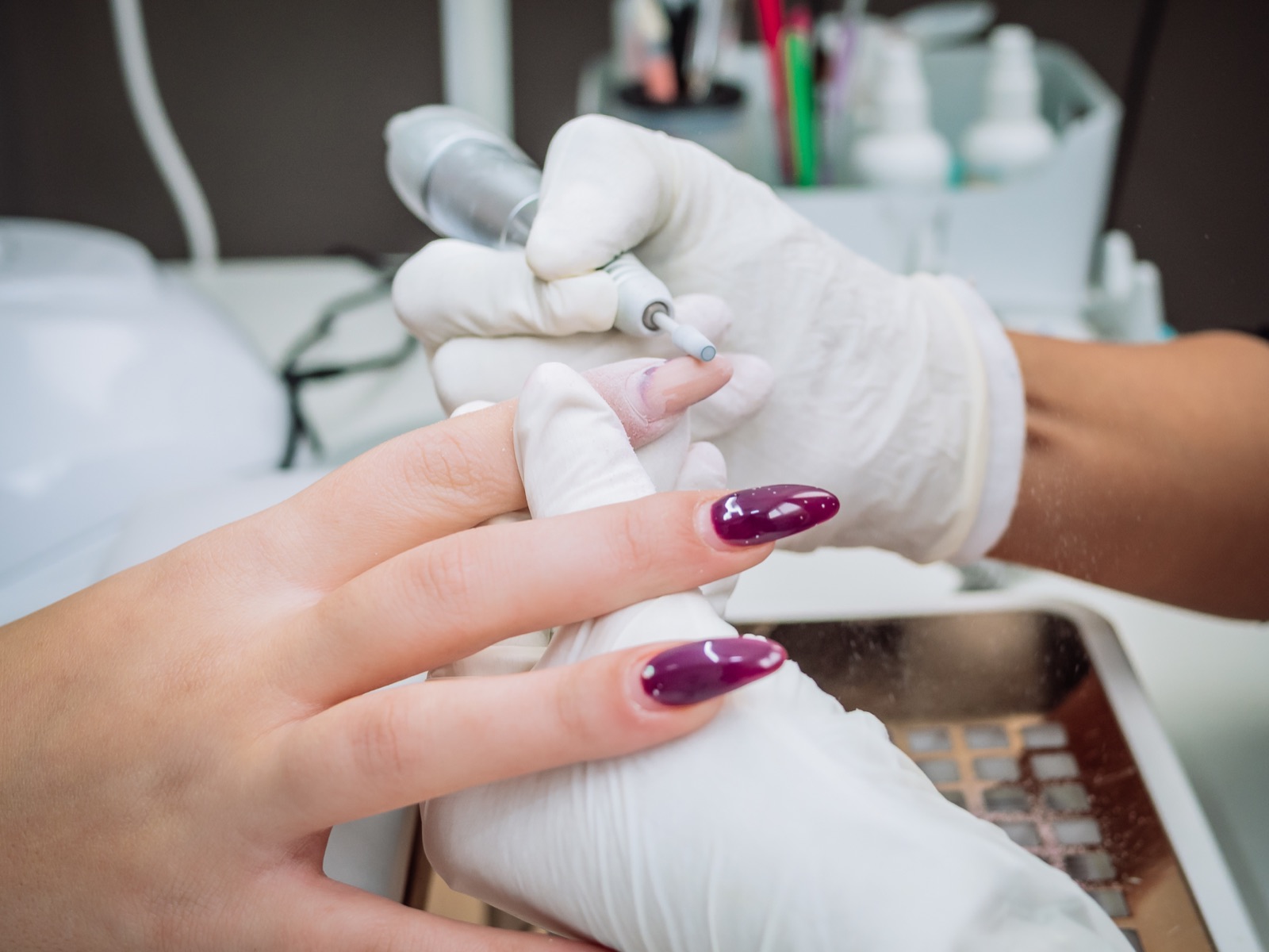 Gloved nail technician using an electric file on a fingernail