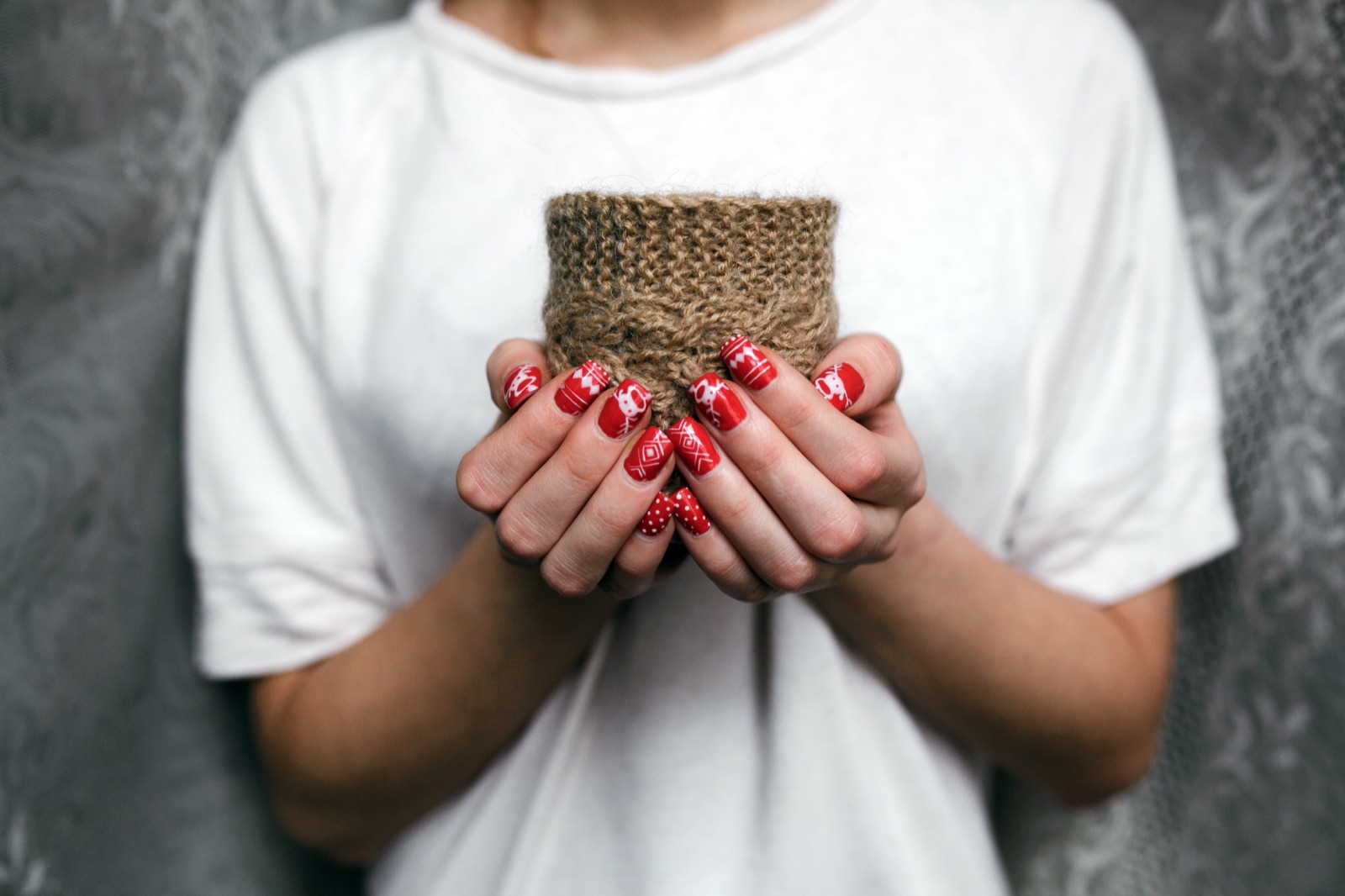 Red nails with white festive patterns around a knitted cup sleeve
