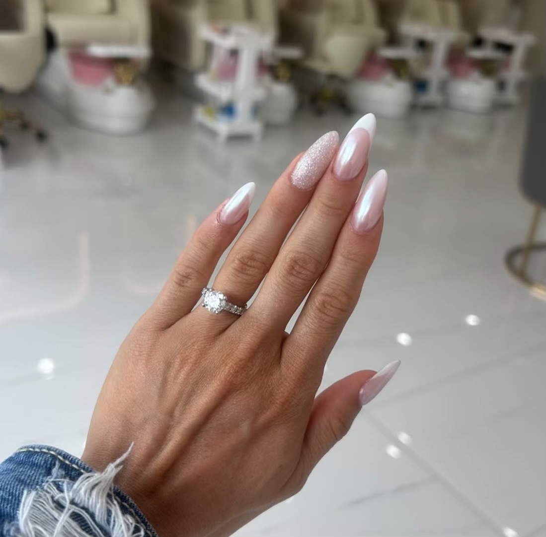 Close-up of pearlescent pink bridal nails with french tips, a glitter accent and an engagement ring