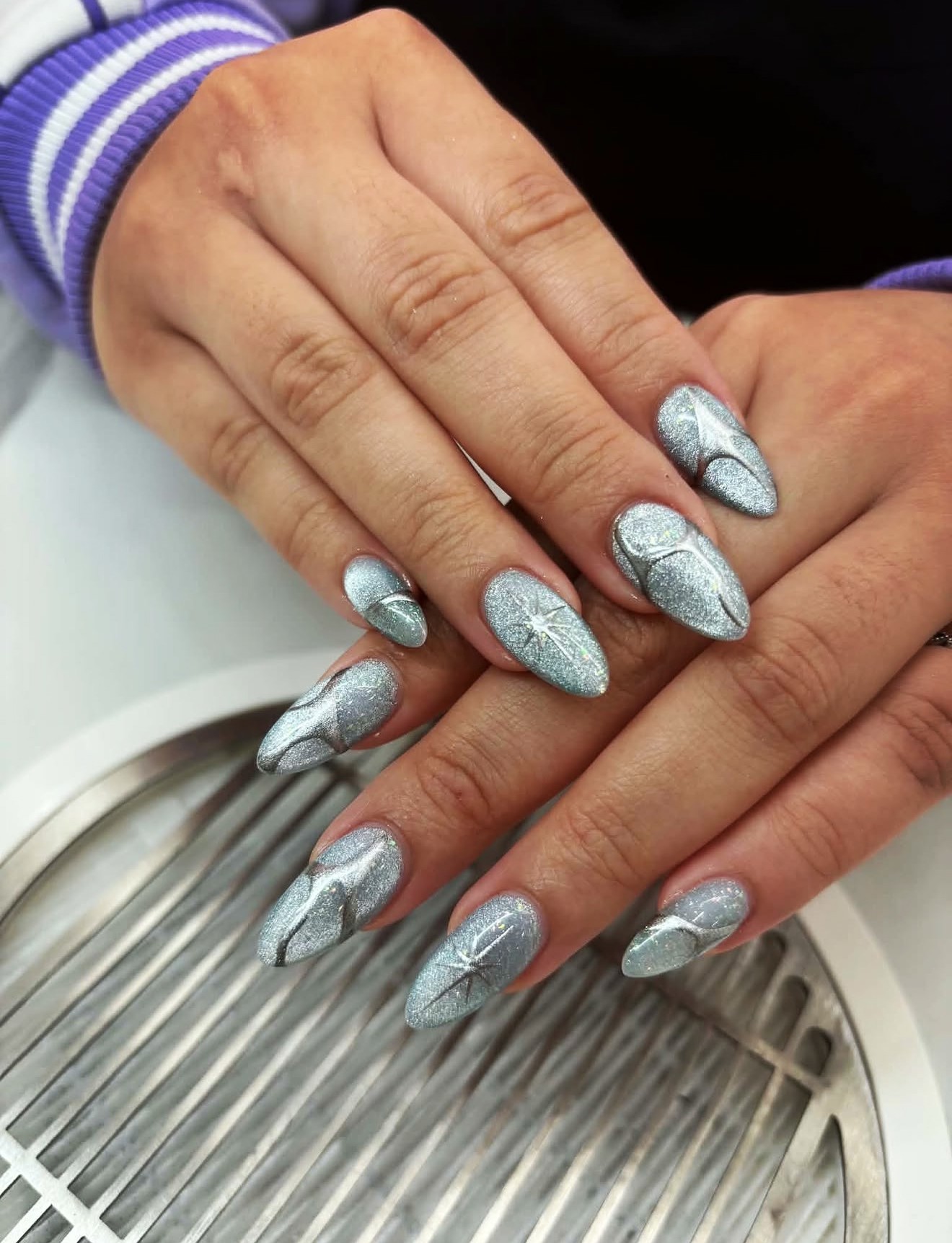 Silver glitter almond nails with star accents and curved line details