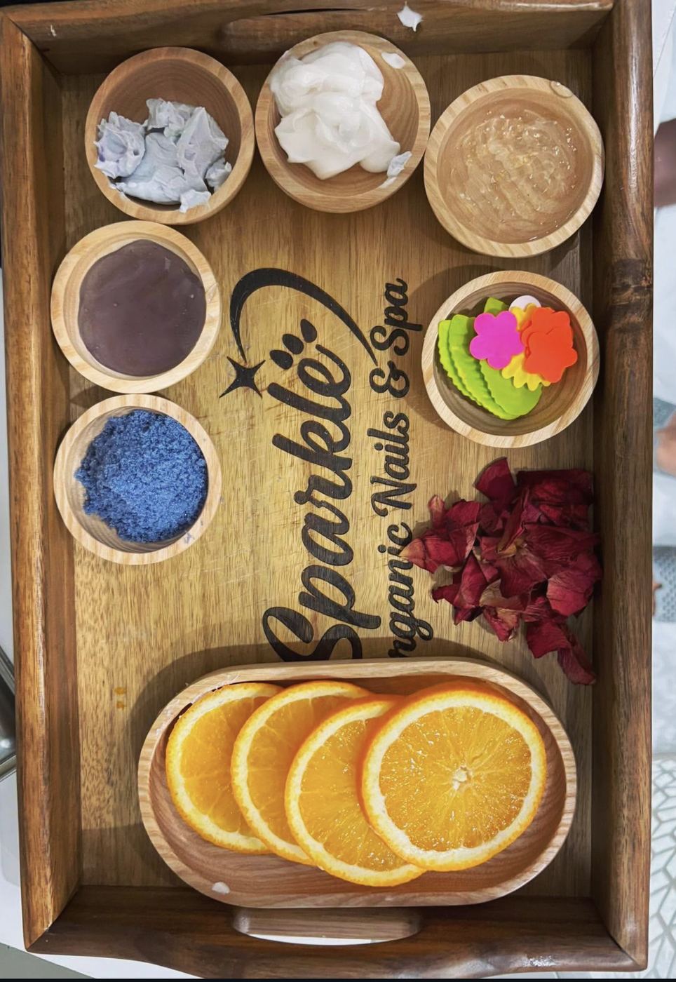 Spa tray with orange slices, rose petals and small wooden bowls.