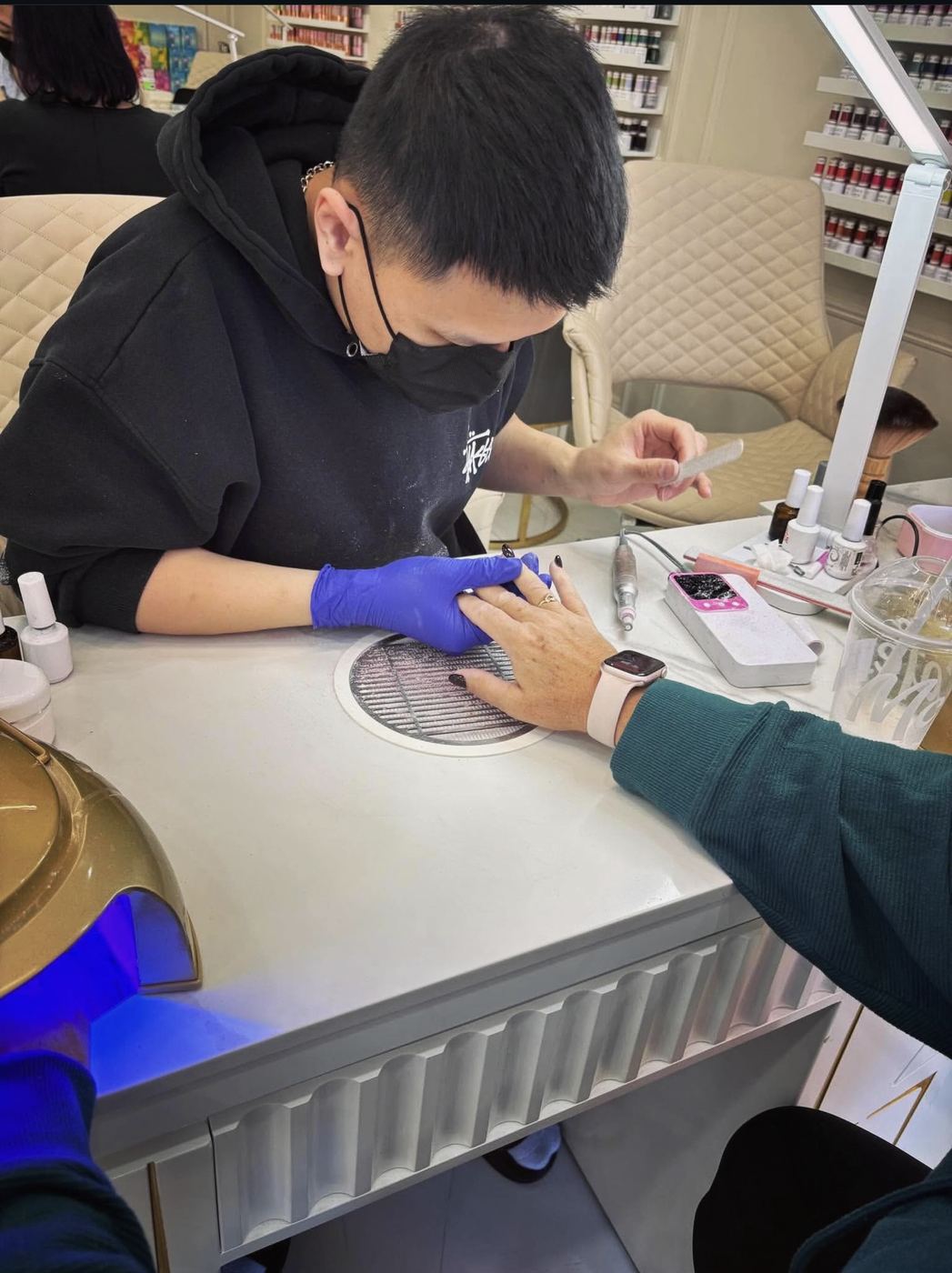 A nail technician holding a file while supporting a client’s hand at a manicure station.