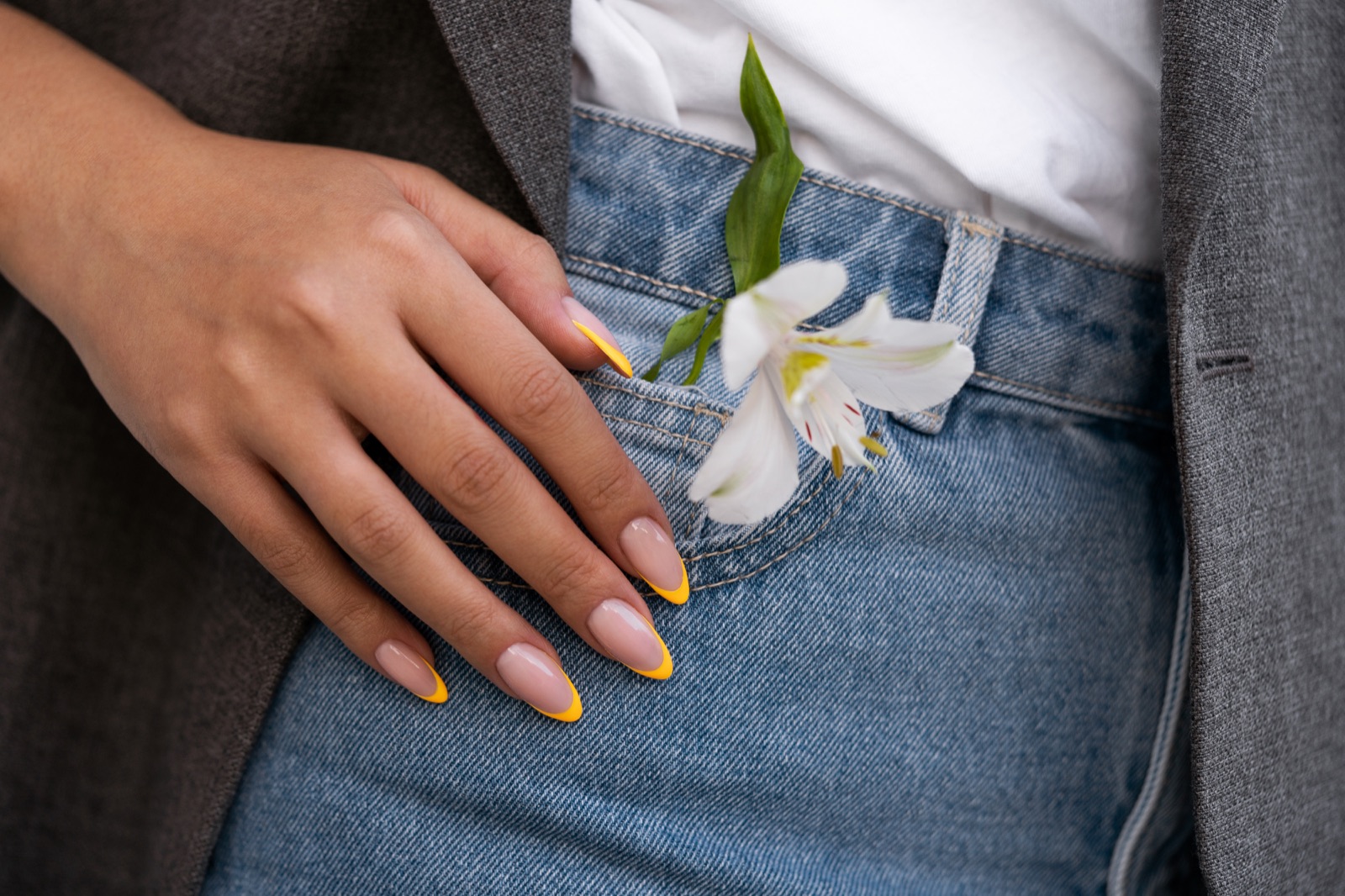 Yellow french-tip nails beside a white flower and blue denim